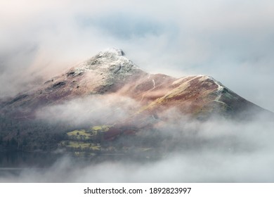 Lake District mountain Catbells covered in low lying misty cloud. Snowcapped moody fell tops.