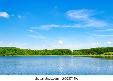 Lake in the forest on a clear summer day. Specular reflection in the water. Green foliage of trees. Coast. Blue sky with white clouds on a sunny day. - Powered by Shutterstock