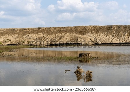 Lake with island and tree stump - rocky cliff with sedimentary layers - calm water and blue sky with clouds