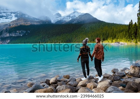 Lake Louise Banff National Park in the Canadian Rocky Mountains. A young couple of men and women standing on a rock by the lake during a cold day in Autumn in Canada watching the sunset