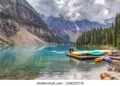 LAKE LOUISE, CANADA - AUG 21, 2014: Visitors taking a cold dip in Moraine Lake near Lake Louise in Banff National Park as friends took pictures. Heavy clouds descend on the mountains background. - Shutterstock ID 1106325776