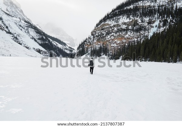 Lake Louise completely\
frozen with people walking on top of it with large rocky mountains\
around it