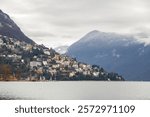 Lake Lugano with hillside architecture on Monte Bre and mist-covered mountains in the background, in Lugano, Switzerland