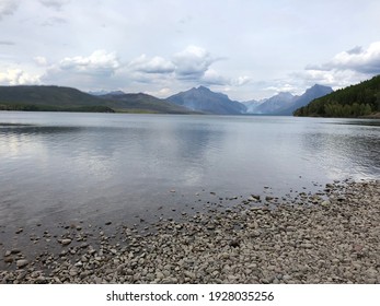 Lake In The Mountains Of Glacier National Park. With A Small Forrest Fire In The Backdrop