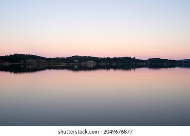 The lake at nightfall. View of the tranquil lake, forest and mountains in the horizon with a beautiful dusk light, reflected on the water surface. 