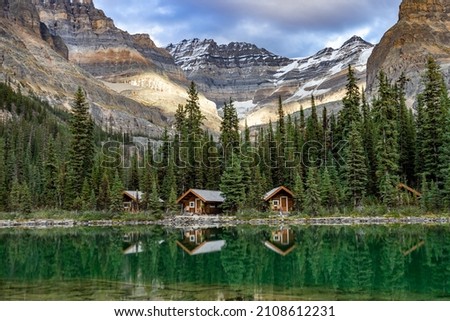 Lake O'Hara cabins reflecting in the emerald water of the lake with mountain peaks in the background, Yoho National Park, Canada.