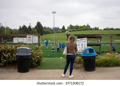 Lake Oswego, OR, USA - May 3, 2021: A Mother Waits Outside The Sports Field And Looks At Her Daughter Taking Part In A Girls Soccer Camp In Lake Oswego, Oregon, During A Pandemic Springtime.