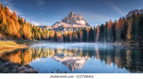 See mit Spiegelbild der Berge bei Sonnenaufgang im Herbst in Dolomiten, Italien. Landschaft mit Antorno See, blauer Nebel über dem Wasser, Bäume mit orangefarbenen Blättern und hohen Felsen im Herbst. Farbiger Wald 