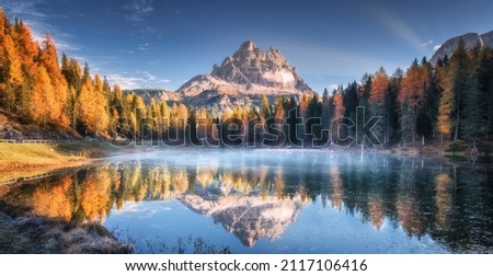 Lake with reflection of mountains at sunrise in autumn in Dolomites, Italy. Landscape with Antorno lake, blue fog over the water, trees with orange leaves and high rocks in fall. Colorful forest 