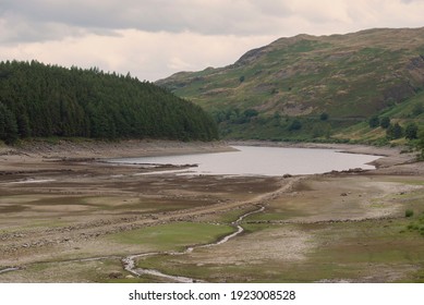Lake reservoir in the summer drought. Haweswater in the UK lake district. Low level of water with ruins visible. Green hills to the sides and in the background.