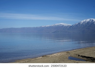 Lake shore with snow capped mountains in the background and blue sky - Powered by Shutterstock