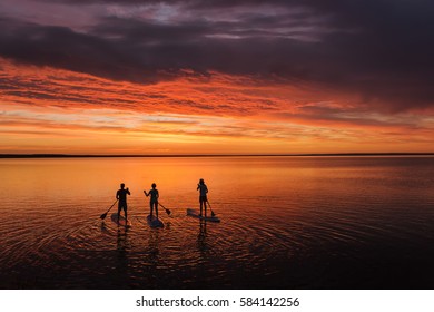 lake sup surfing under amazing dark sunset sky with three people
