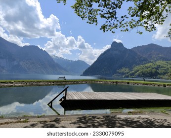 Lake Traunsee in Austrian Alps. Green mountains. Blue sky and white clouds. Reflection in crystal clear water. Wooden bench on a lake coastline. Boathouse at a lake.