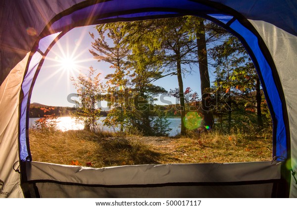 Lake view from inside of a tent . Camping\
upstate New York. Sunset light, lens flare. The Catskills are one\
of the most popular destination for scenic drives, bike trails,\
foliage and nature lovers.\
