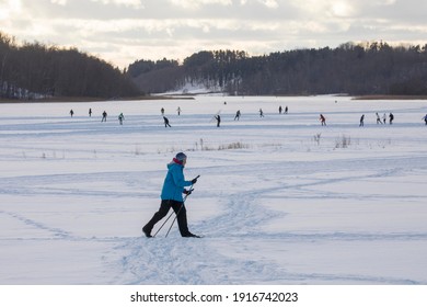 Lake Viljandi, Viljandi, Estonia - 02.14.2021: Female Person Exercising Cross-country Skiing On The Frozen Lake Ice Sheet With The Background Of The Distant Skaters In The Crisp Sunny Winter Day