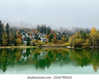 lakeside alpine village in autumn forest. vibrant fall colors. water refrection. misty hills. cozy cottages. atmospheric. autumn background. fall aesthetic - Powered by Shutterstock