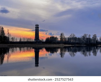 A lakeside lighthouse is reflected in the water at sunset. - Powered by Shutterstock