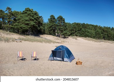 Lakeside sandy beach with chairs, picnic basket and dome tent. - Powered by Shutterstock