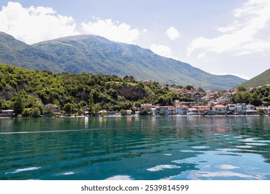 Lakeside town Trpejca nestled amidst lush green mountains of National Park Galicica, North Macedonia. Serene scene along shoreline of Lake Ohrid. Boat trip summer vacation. Balkan travel destination - Powered by Shutterstock