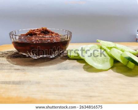Lalap or raw vegetable containing cucumber and spicy chili sauce on a wooden plate, isolated with white background. One of healthy Indonesian dish that usually eaten as an accompaniment to fried dish
