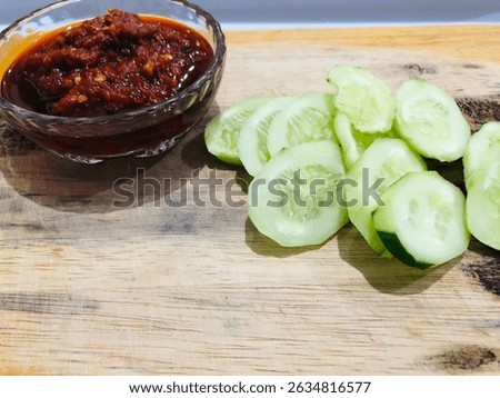Lalap or raw vegetable containing cucumber and spicy chili sauce on a wooden plate, isolated with white background. One of healthy Indonesian dish that usually eaten as an accompaniment to fried dish