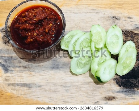 Lalap or raw vegetable containing cucumber and spicy chili sauce on a wooden plate, isolated with white background. One of healthy Indonesian dish that usually eaten as an accompaniment to fried dish