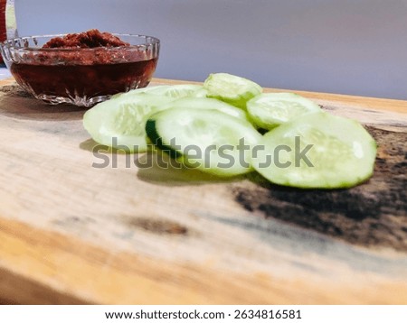 Lalap or raw vegetable containing cucumber and spicy chili sauce on a wooden plate, isolated with white background. One of healthy Indonesian dish that usually eaten as an accompaniment to fried dish
