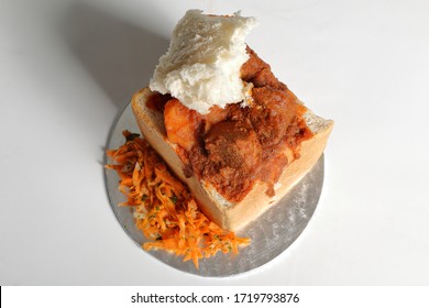 A lamb "bunny chow" - the popular, Indian fast food cuisine which originated in South Africa. Consists of lamb curry in a hollowed-out loaf of white bread. Served with carrot salad. - Shutterstock ID 1719793876