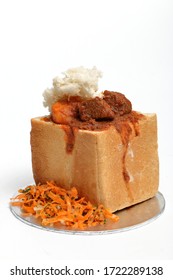 A lamb "bunny chow" - the popular, Indian fast food cuisine which originated in South Africa. Consists of lamb curry in a hollowed-out loaf of white bread. Served with carrot salad. - Shutterstock ID 1722289138