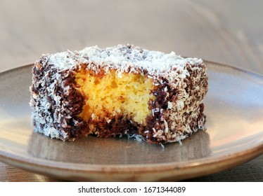 Lamington cake closeup with a bite missing. Squares of sponge cake coated in chocolate sauce and rolled in desiccated coconut