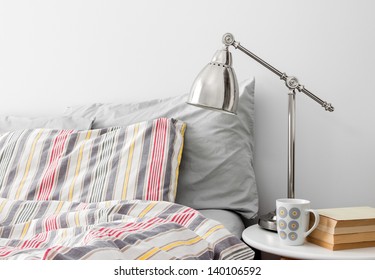 Lamp And Books On A Side Table Near Bed With Colorful Bed Linen.