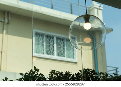 A lamp with a bulb in a glass globe hangs over a window. The lamp is lit up, and the window is open. The scene is bright and cheerful, with the sunlight streaming in through the window - Powered by Shutterstock