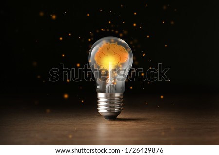 Lamp bulb with shining brain inside on wooden table against black background. Idea generation
