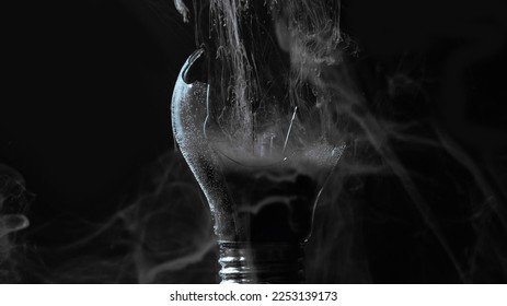 Lamp explosion smoke cloud. Power failure. Defocused gray color vapor haze in broken glass light bulb on dark black night abstract background.