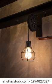 A lamp with a metal frame hanging in a London pub. The lamp is attached to an old pulley.