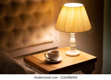 Lamp. Night light by the bedside table with warm light. Intimate setting. Lamp for reading a book on the bed. Bedside table with night light.Tea in bed