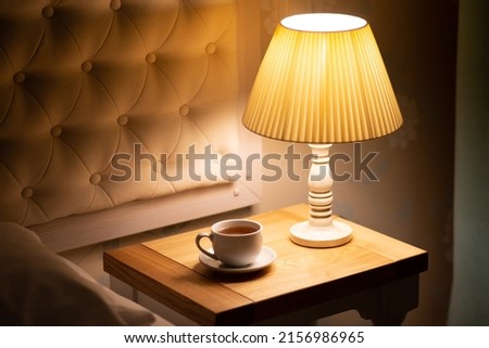 Lamp. Night light by the bedside table with warm light. Intimate setting. Lamp for reading a book on the bed. Bedside table with night light.Tea in bed
