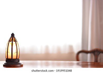 “art deco” lamp.  put on a walnut oval dining table.
window is bright. 

This expensive antique furniture is made in England. 
clear background with soft focus image.