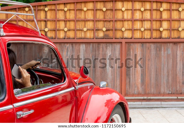 LAMPANG THAILAND - AUGUST 27 2018 : Woman in red\
Volkswagen car, hand using remote control to open the automatic\
gate while phoning and leaving home.Security and save time,\
wireless technology\
concept