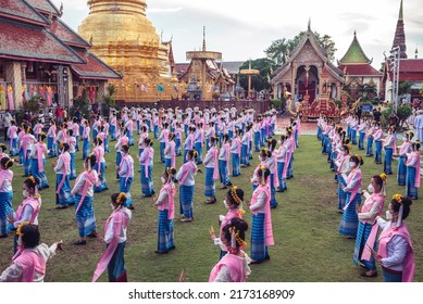 LAMPHUN, THAILAND - MAY 9, 2022: Group of female dancers wearing long nails dressed in traditional robes clad in pink leaves dance during the annual Phrathat Bathing Festival 