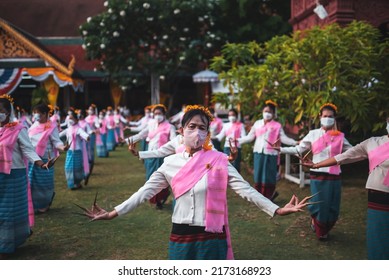 LAMPHUN, THAILAND - MAY 9, 2022: Group of female dancers wearing long nails dressed in traditional robes clad in pink leaves dance during the annual Phrathat Bathing Festival 