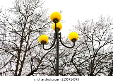 A Lamppost With Yellow Round Lamp Shades.