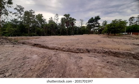 Land equalization, white soil, empty space, no green trees, no grass, bright sky. There are a few mango trees.