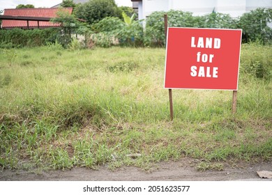 Land For Sale Sign. Red Sign For Sale Plot. Green Lawn Behind Sign. Land For Sale Signboard On Street Signs. Buying Plot Building A House. Signboard Of Realtor Or Real Estate Agent.