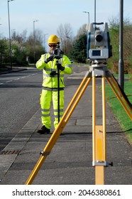 Land surveyor performing initial survey of the road levels and kerb lines before start of construction works using robotic tacheometer controlled by remote control and prism on pogo. - Shutterstock ID 2046380861