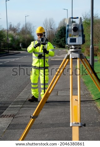 Land surveyor performing initial survey of the road levels and kerb lines before start of construction works using robotic tacheometer controlled by remote control and prism on pogo.