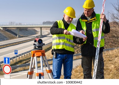 Land surveyors on highway reading geodesist plans use tacheometer