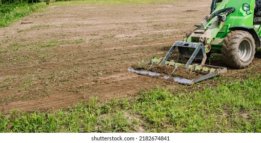 Land work by the territory improvement. Small tractor with a ground leveler for moving soil, turf. A green mini skid steer loader clear the construction site. Machine for agriculture work. Copy space.