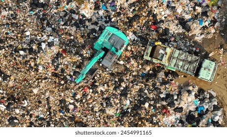 A landfill sprawls, a mosaic of refuse. A teal excavator toils beside a truck, amidst the chaos of mixed waste. The scene echoes humanity's consumption and the tireless effort of waste management.  
