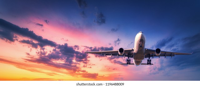 Landing airplane against colorful sky at sunset. Landscape with aircraft is flying in the blue sky with orange and pink clouds. Travel background with passenger plane. Commercial airplane. Private jet